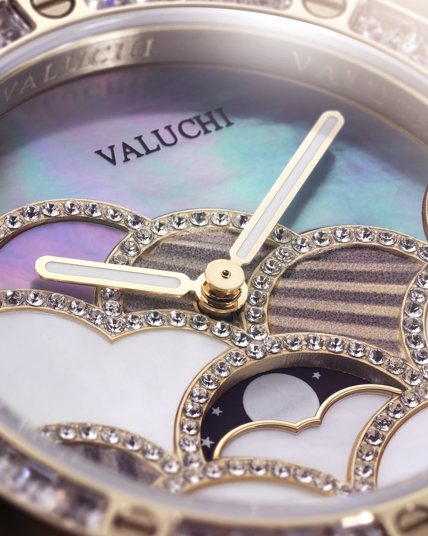 Close-up of a Valuchi watch dial with gold-tone hands, iridescent mother-of-pearl background, crystal-encrusted moonphase-style cutouts, and a silver-toned bezel.